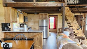A cozy cabin-style interior with a wooden dining table, a sofa, and a kitchen area with a refrigerator and a stove.