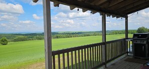 A covered outdoor area with a view of a green field and distant hills.