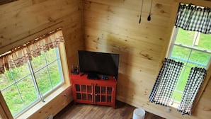 A cozy cabin interior with a sofa, a small table, and a TV on a red cabinet.