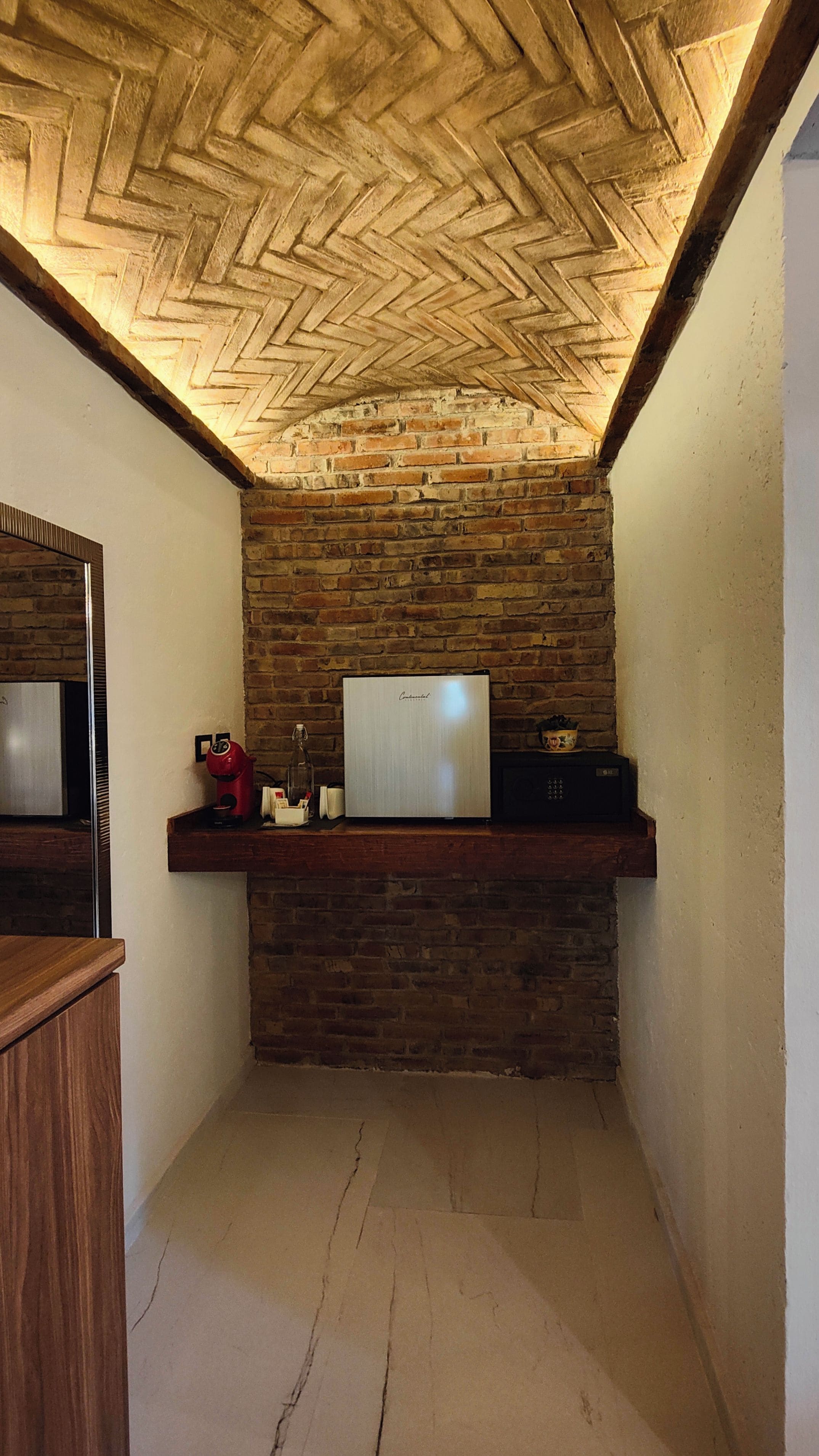 A room with a brick wall, a wooden ceiling with a herringbone pattern, a white refrigerator, and a wooden counter with a red appliance.