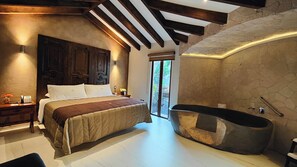 Une chambre à coucher avec un grand lit, une tête de lit en bois, une table de chevet avec un téléphone et un vase, et une salle de bain avec une baignoire.