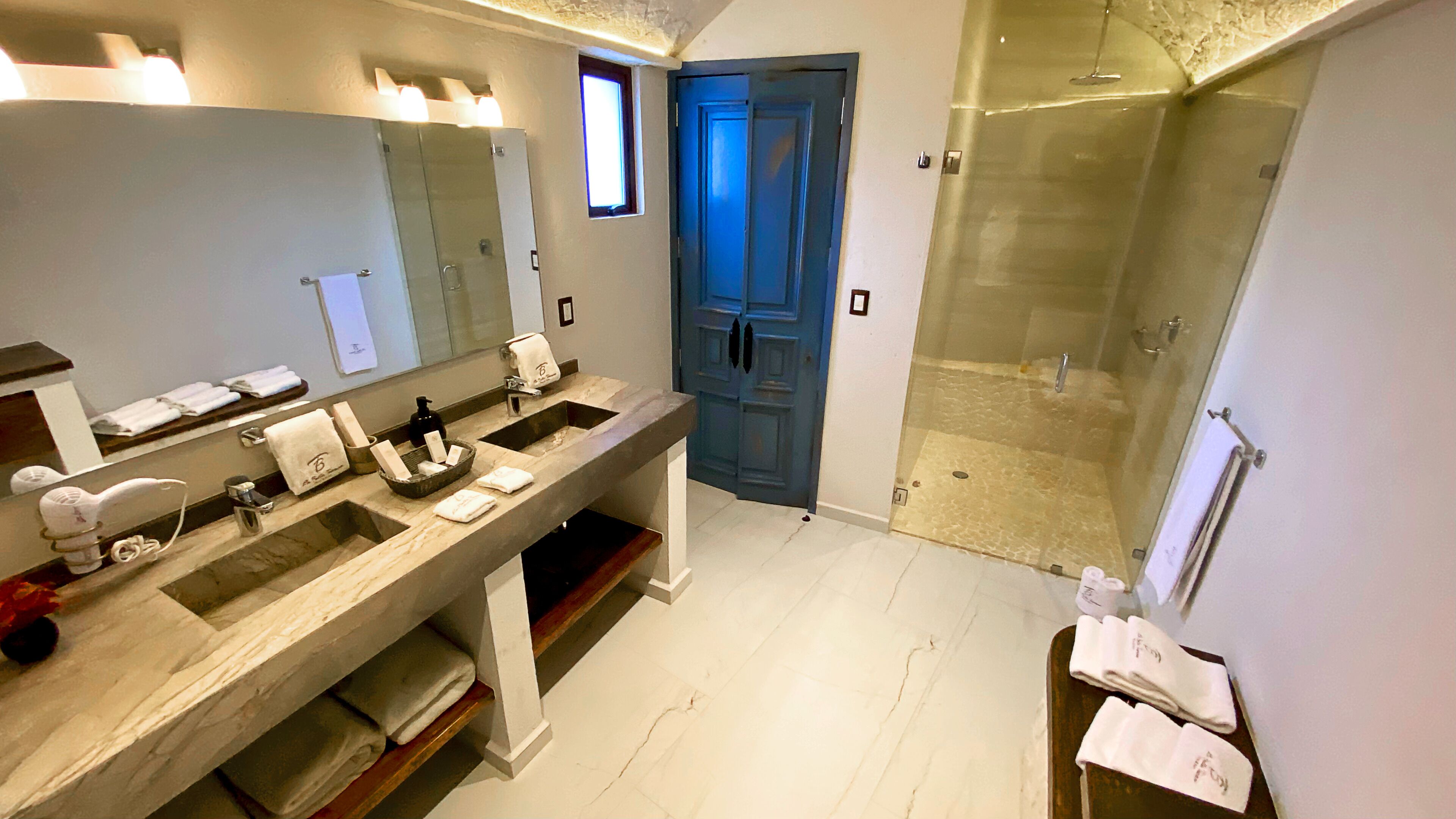 A modern bathroom with two sinks, a large mirror, and a glass-enclosed shower.