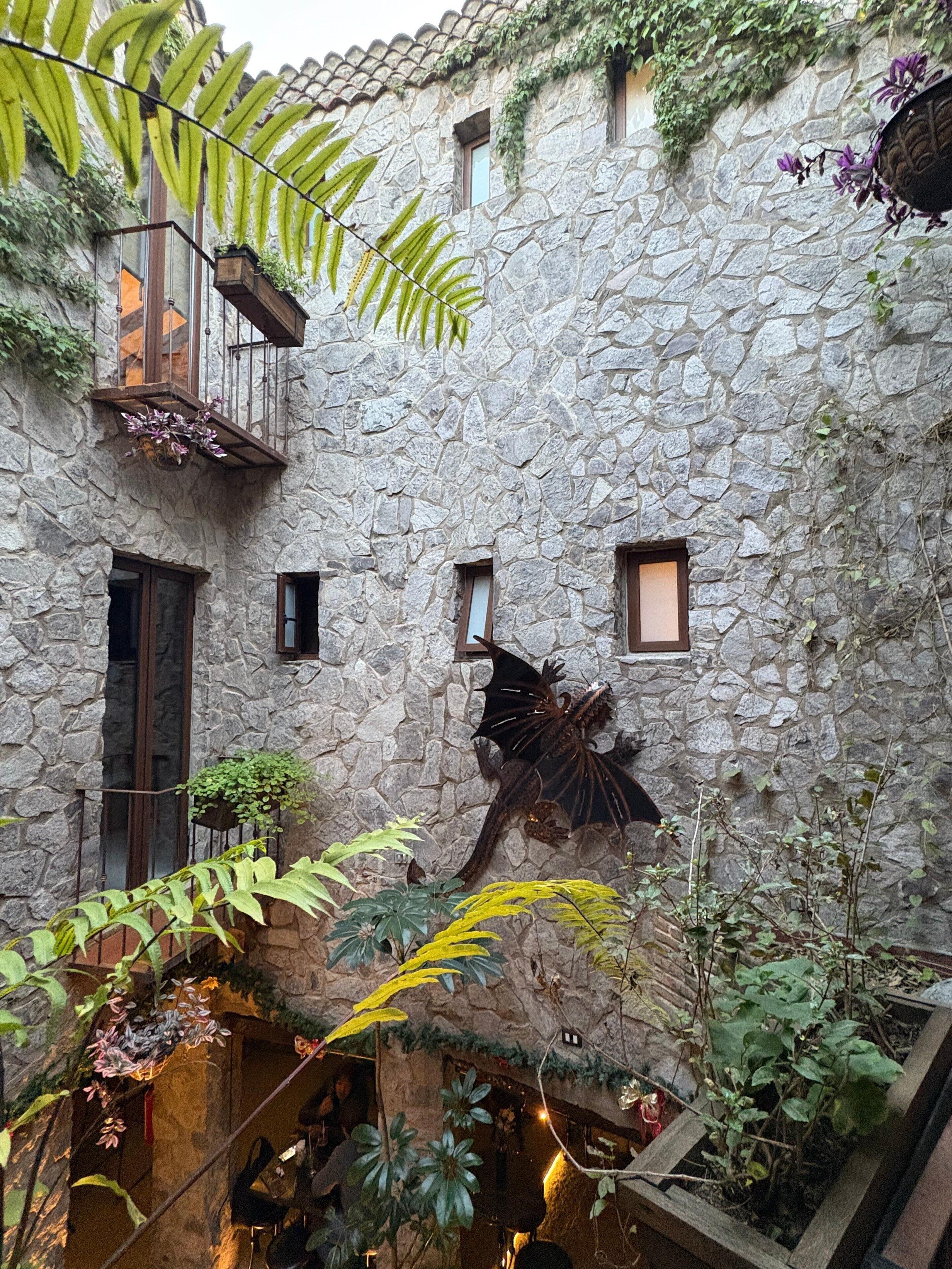 Un edificio de piedra con numerosas ventanas y balcones, rodeado de exuberante vegetación y plantas.