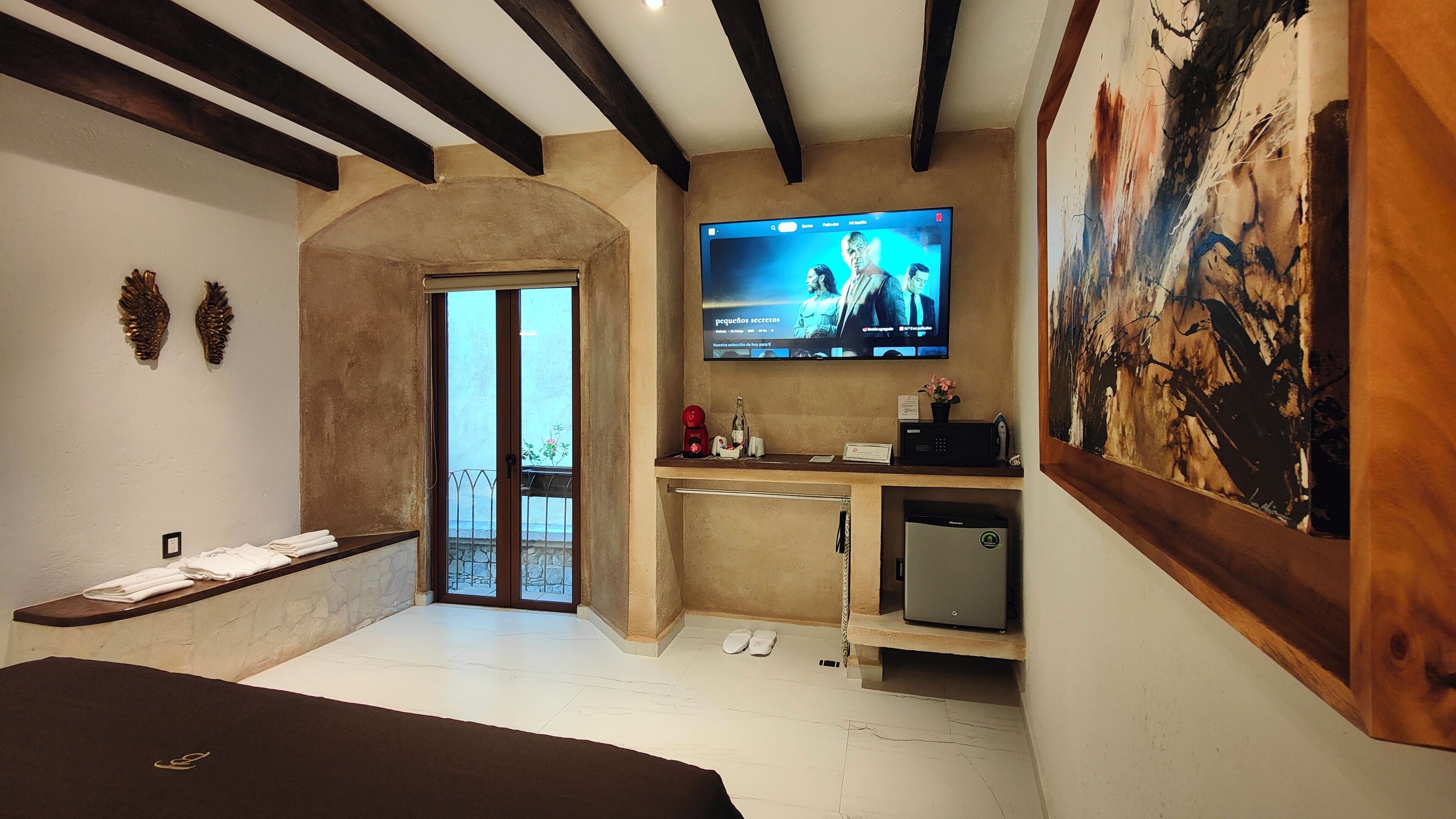 Habitación de hotel con televisor grande, minibar, refrigerador pequeño y balcón con vistas.