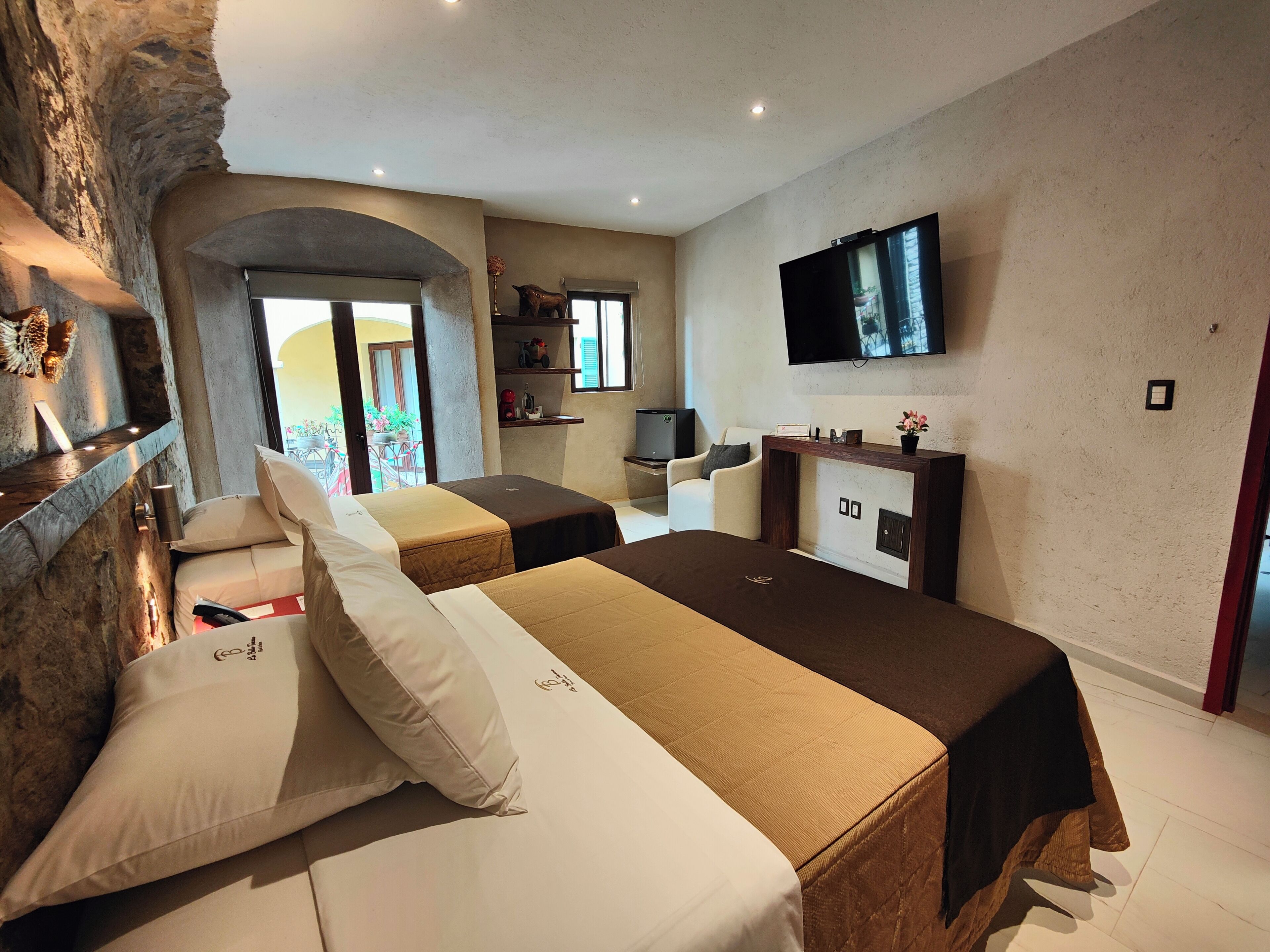 A hotel room with two beds, a TV, a fireplace, and a stone wall.