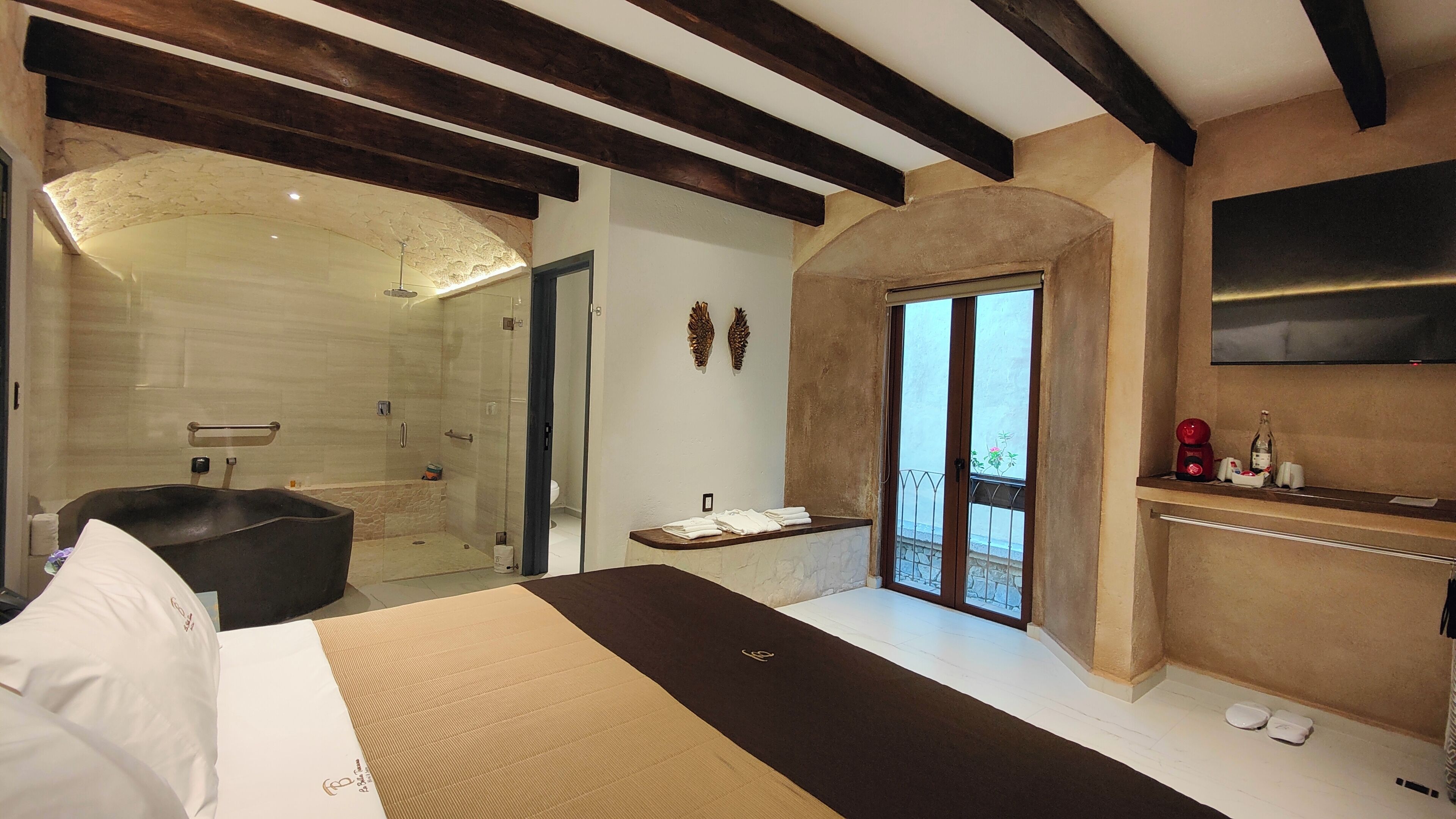 Ein modernes Schlafzimmer mit einem großen Bett, einer Duschkabine, einem Balkon mit Blick und einem angebrachten Fernseher.