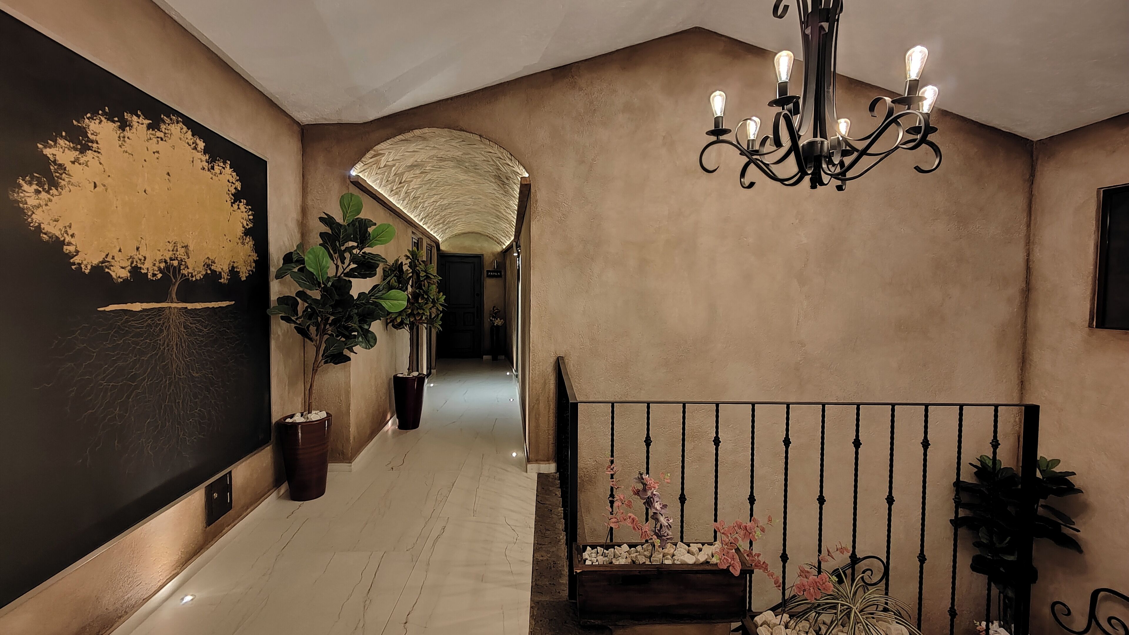 A hallway with a chandelier, potted plants, and a large abstract painting on the wall.
