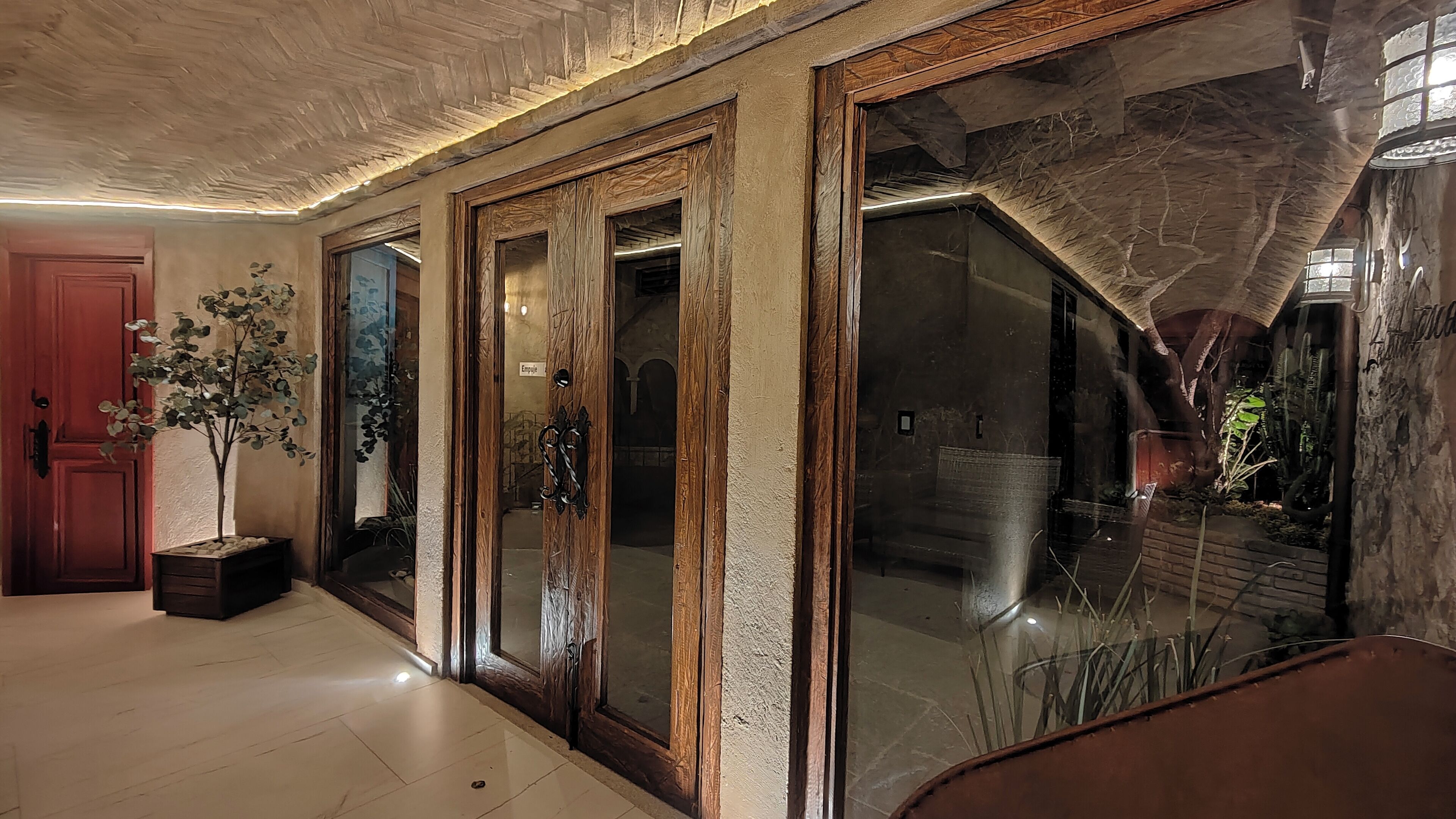 Un pasillo con puertas de madera, una planta en maceta y una escalera que sube a un nivel superior.