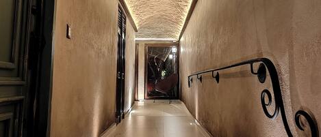 Un couloir avec un plafond orné d’un motif en chevrons, un sol en marbre et une balustrade en métal.