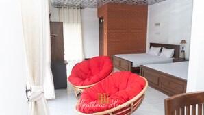 Una habitación de hotel con dos camas individuales, un sillón rojo acolchado, una mesita de noche de madera y una cortina blanca.