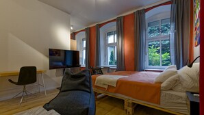 Une chambre d’hôtel comprenant un lit, un bureau avec une chaise, une télévision et de grandes fenêtres avec des rideaux.
