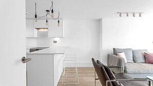 A modern kitchen with white cabinetry, a bar area, and a seating area with a sofa and chairs. - Belgravia Base: 2BR Near Victoria/Sloane (London)