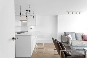 A modern kitchen with white cabinetry, a bar area, and a seating area with a sofa and chairs. - Belgravia Base: 2BR Near Victoria/Sloane (London)