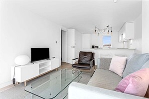 Una sala de estar moderna con un televisor de pantalla plana, una mesa de centro de vidrio, un sillón de cuero y un sofá con cojines.
