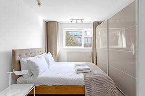 A hotel room with a bed, a bedside table, a window, and a view of the outside.