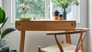 Een kamer met een groot raam, een houten bureau, een stoel en een potplant.