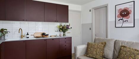Une cuisine moderne avec des meubles de couleur sombre, un plan de travail blanc et un canapé gris agrémenté de coussins à motifs.