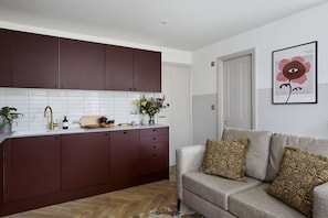 Modern kitchen with a stainless steel faucet and a living area featuring a light grey sofa and framed artwork.