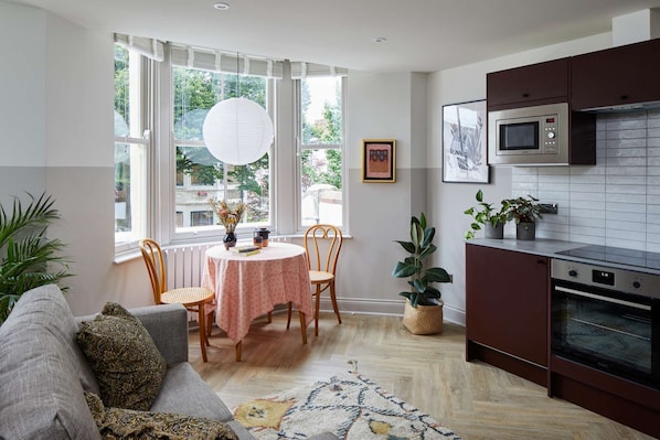 Cozy living space with a sofa, round table, and kitchen area featuring a microwave and oven.