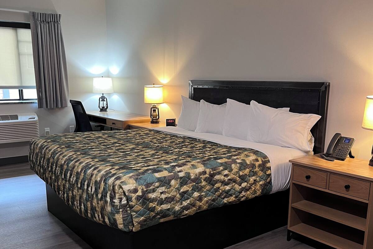 A hotel room with a bed, a desk, a lamp, a phone, and a wall-mounted air conditioner.