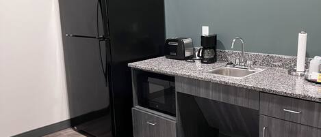 Cocina moderna con un refrigerador negro, horno empotrado, pileta y encimera con tostadora y cafetera.