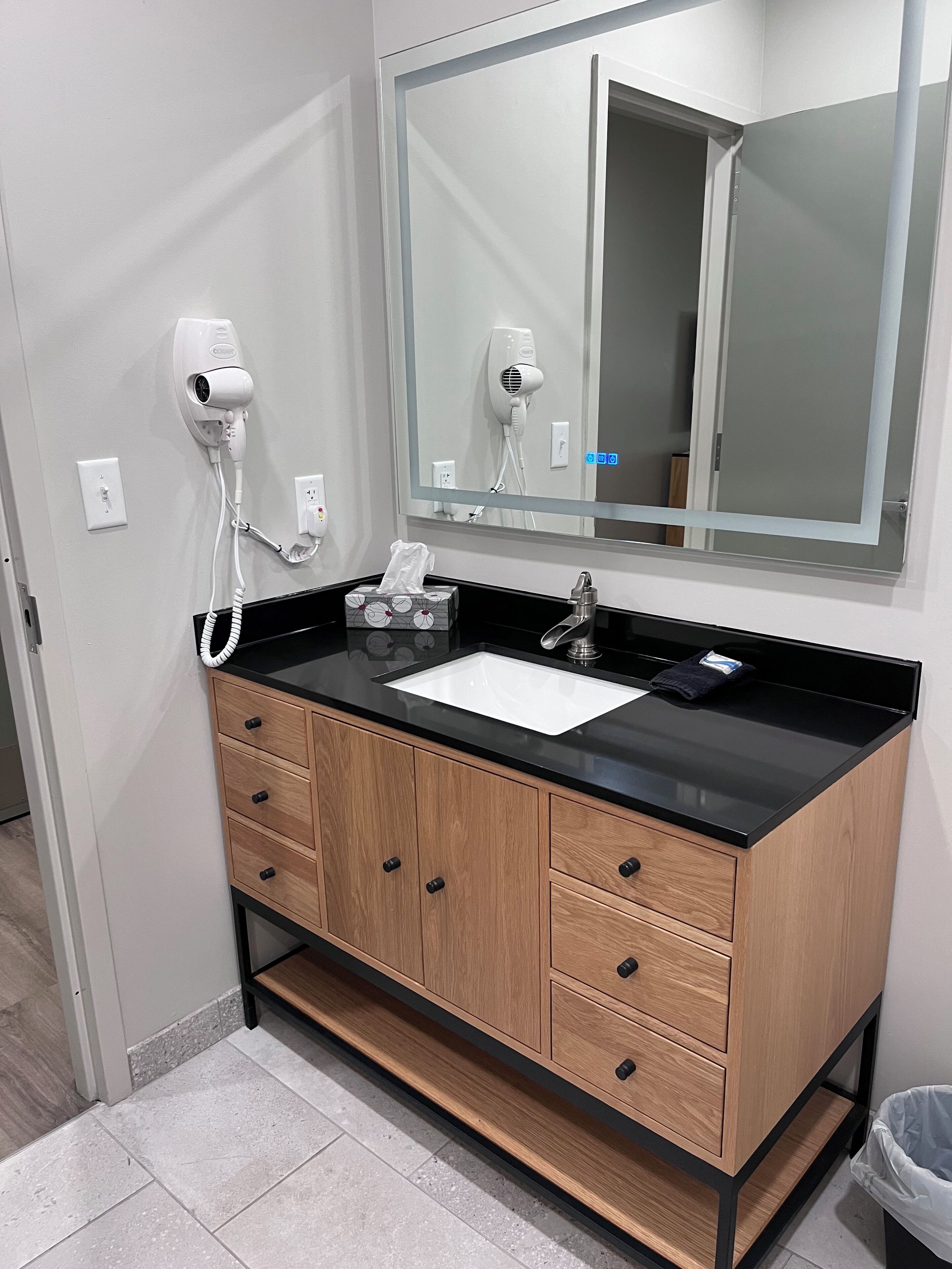 A bathroom with a black countertop, a white sink, a mirror, and a hairdryer.