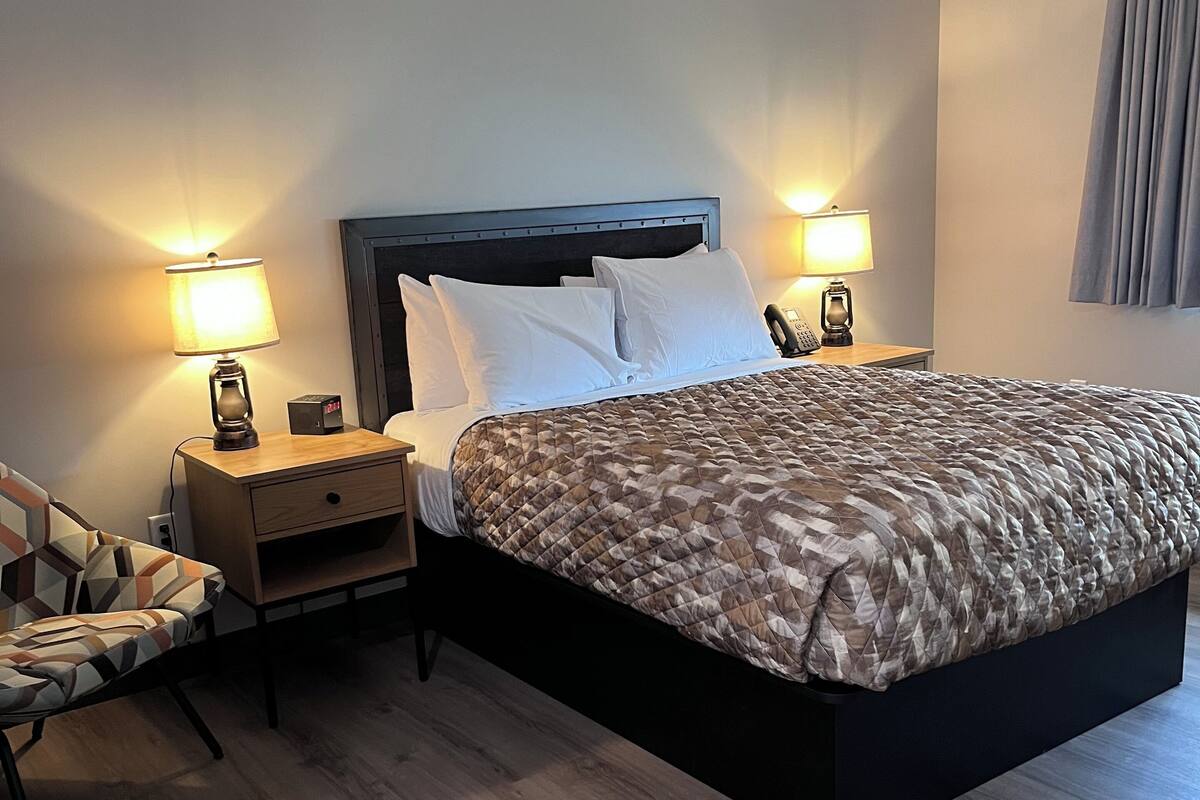 A hotel room with a large bed, two bedside tables with lamps, a chair, and a wooden nightstand.