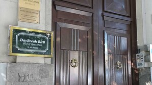 Una gran puerta doble de madera con un picaporte de latón, flanqueada por dos placas y un letrero de DayBreak B&B.