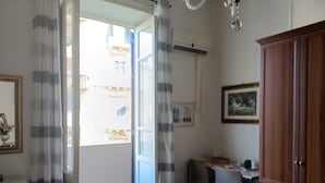 Una habitación con un armario de madera, un escritorio y una silla. Hay una ventana con cortinas, y una puerta que da al exterior.