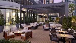 An outdoor seating area with sofas, chairs, and tables, surrounded by potted plants and modern architecture. - Embassy Suites By Hilton Dubai Business Bay (Dubai)