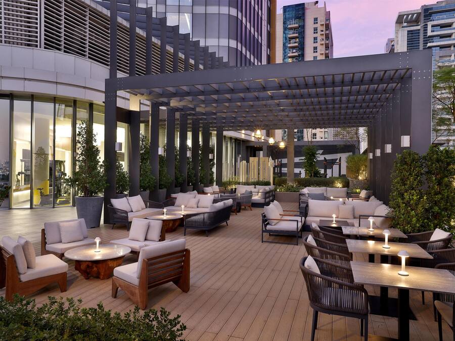 Een buitenzitplaats met banken, stoelen en tafels, omringd door potplanten en moderne architectuur.