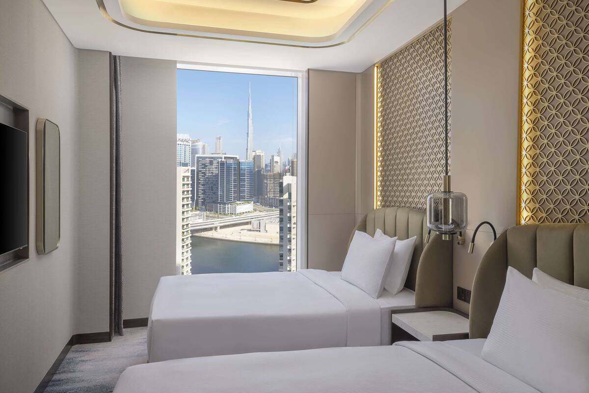 Ein Hotelzimmer mit großem Fenster und Blick auf die Stadt, einem Bett, einem Nachttisch und einer modernen Lampe.