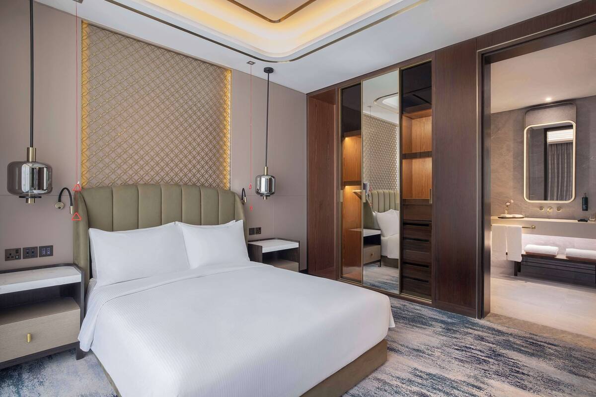 Ein modernes Hotelzimmer mit einem großen Bett, Nachttischen, einem Spiegel und einem Badezimmer mit Badewanne und Waschbecken.
