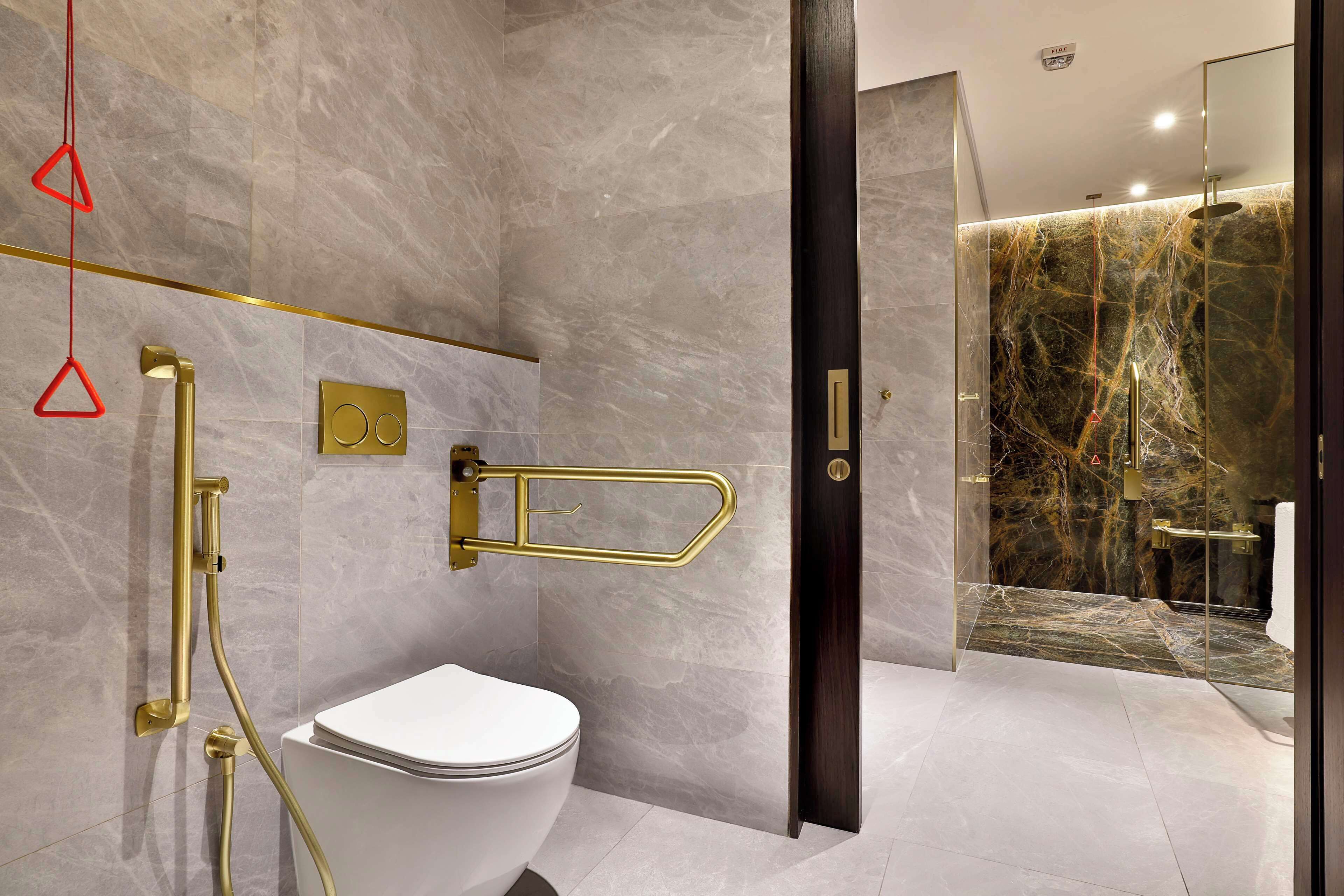 Un baño moderno con inodoro blanco, detalles dorados y paredes de mármol.