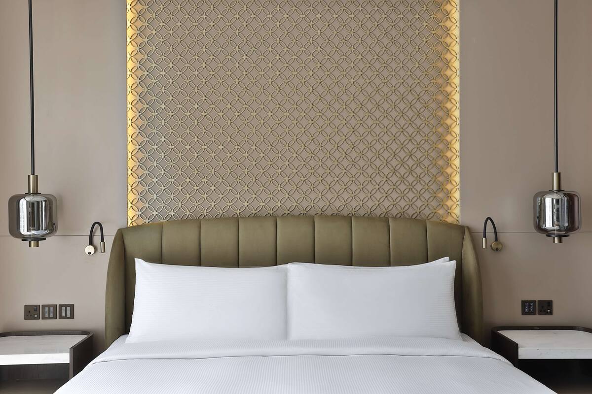Ein Hotelzimmer mit einem großen Bett, zwei Nachttischen, einer Wand mit geometrischem Muster und Pendelleuchten.