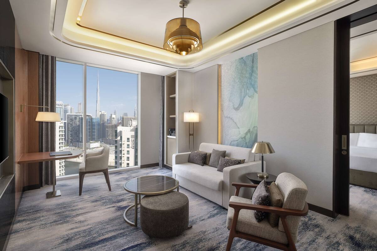 Ein modernes Hotelzimmer mit großem Fenster und Blick auf die Stadt, einem Sofa, einem Couchtisch und einem Fernseher.
