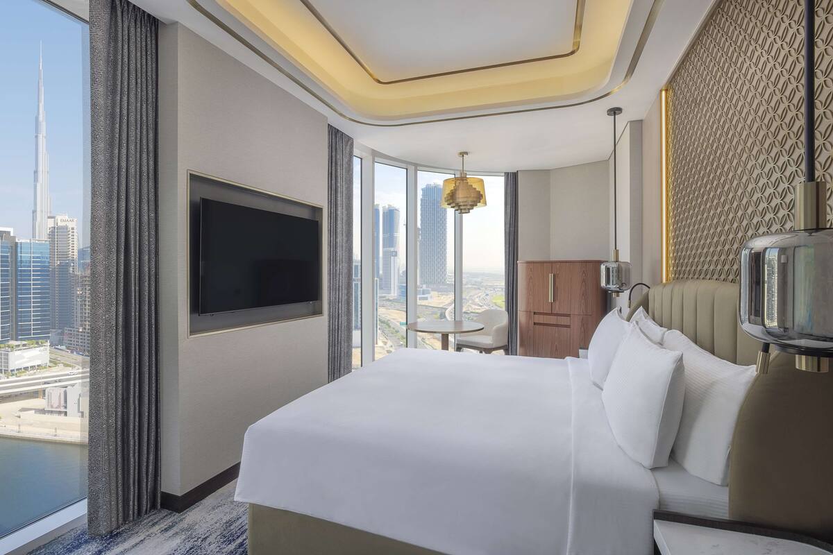 Ein Hotelzimmer mit einem großen Bett, einem Fernseher, einem Esstisch und Blick auf die Stadt.