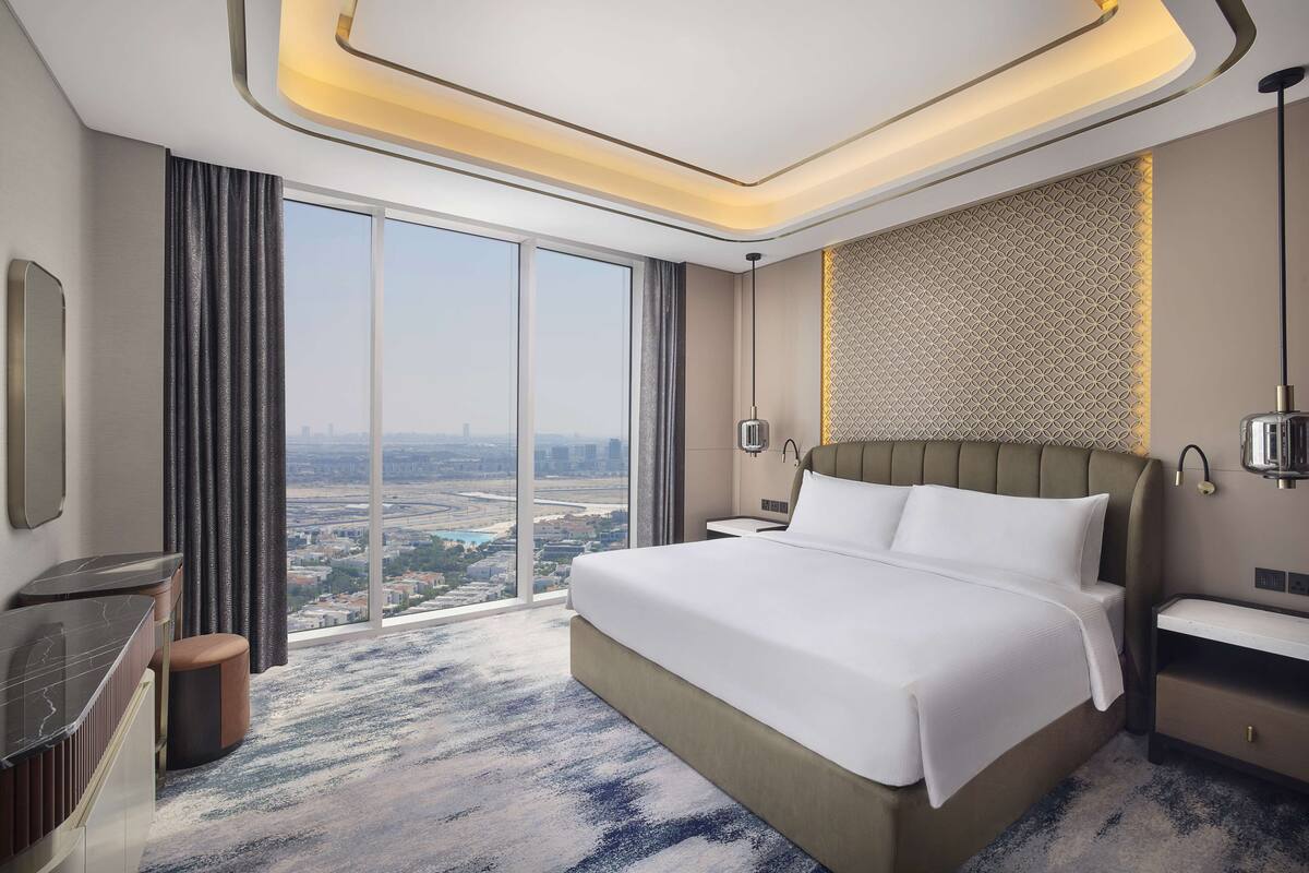 Ein modernes Hotelzimmer mit einem großen Bett, einem Schreibtisch, einem Sessel und Blick auf die Stadt.