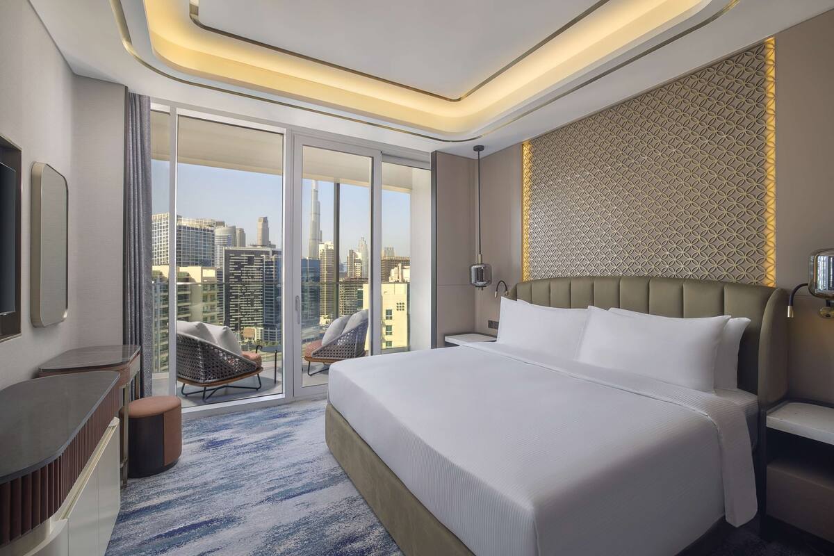 Ein modernes Hotelzimmer mit einem großen Bett, einer Sitzecke mit Blick auf die Stadt und einem Balkon mit einem Stuhl.