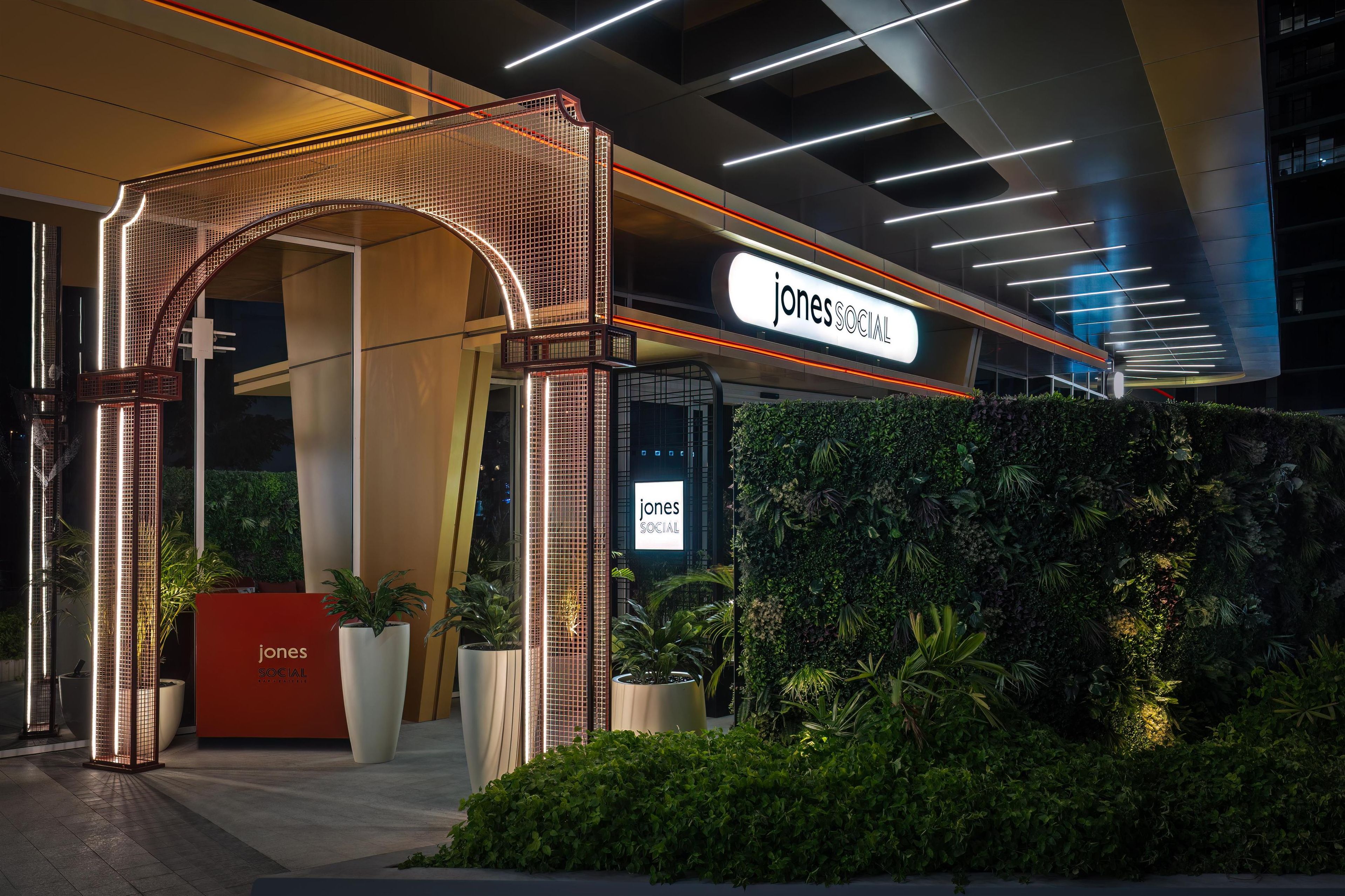A modern building entrance with a 'Jones Social' sign, a red reception desk, and a green wall with plants.