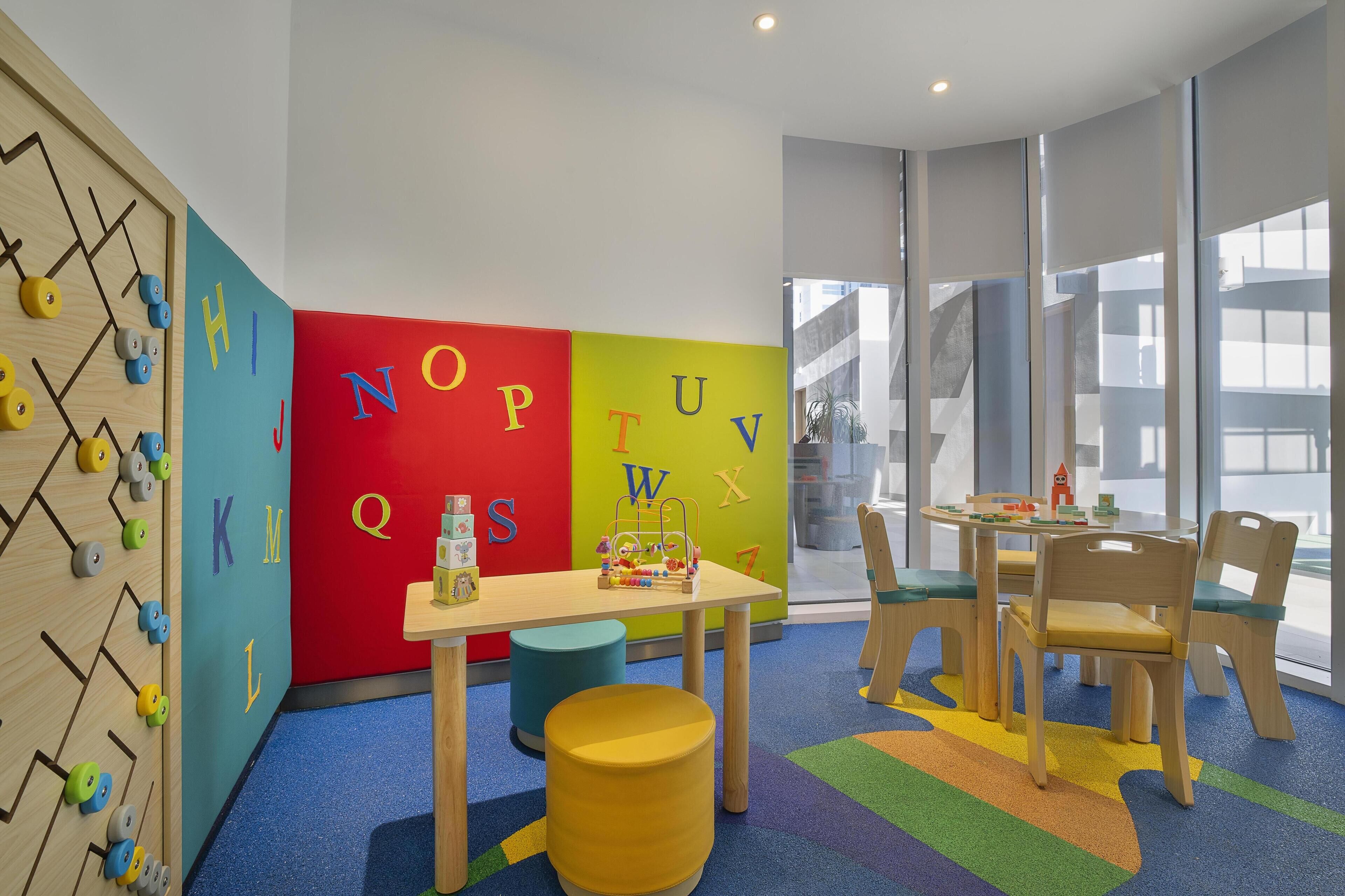 A children's play area with alphabet letters on the wall, a climbing wall, and a table with toys.