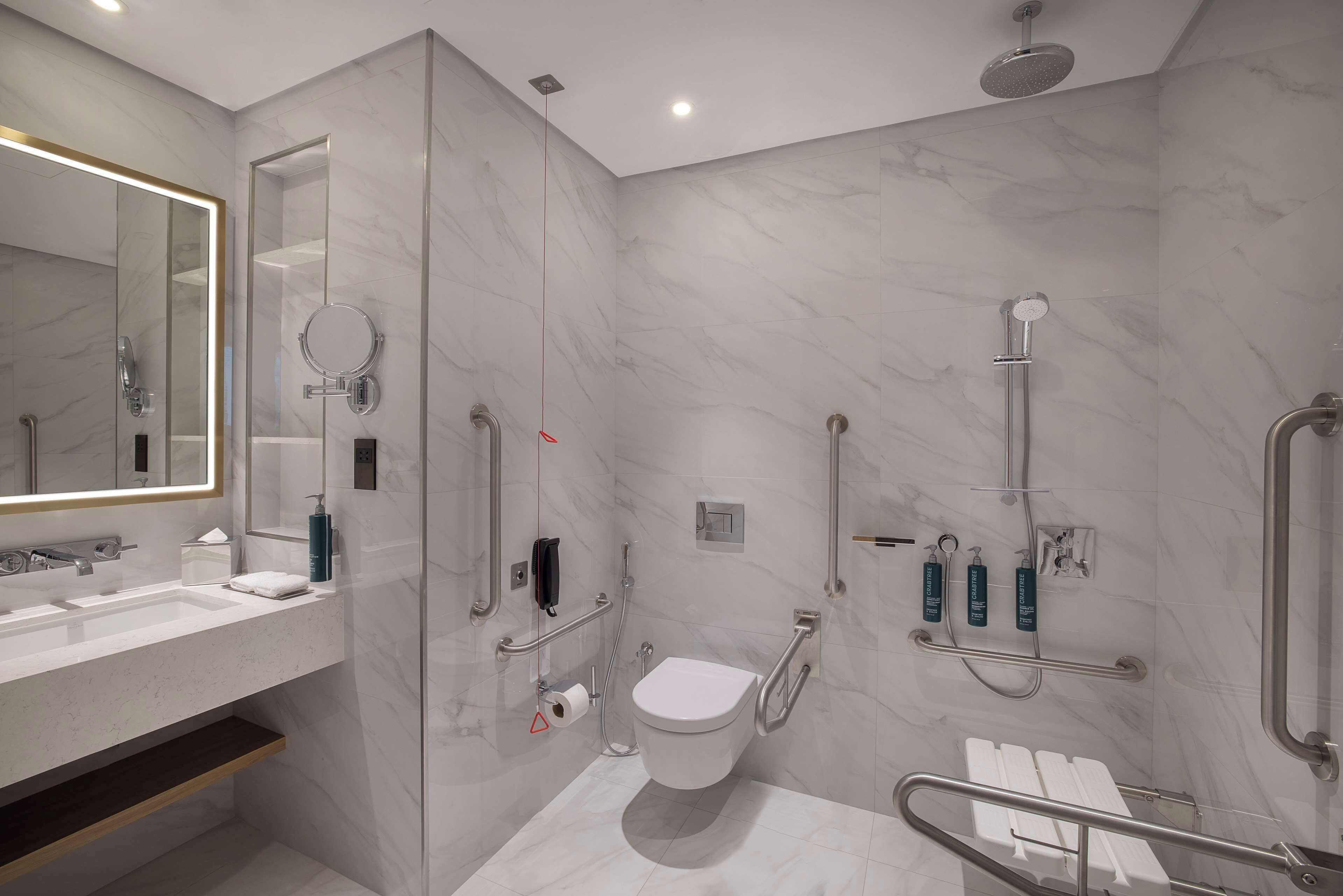 A modern bathroom with a marble floor, a large mirror, a toilet, and a shower area.