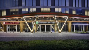 Entrada de hotel con letreros de 'Hilton Garden Inn' y 'Embassy Suites', diseño moderno con puertas de cristal y un camino pavimentado.