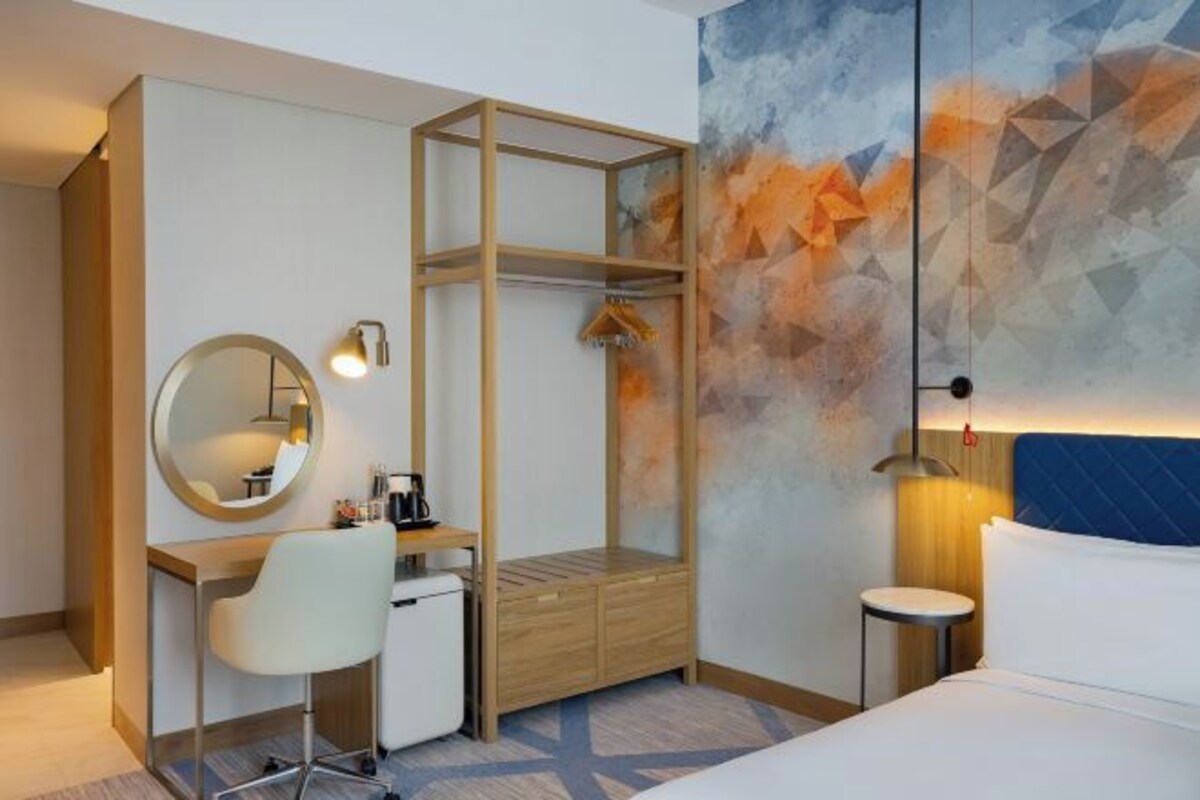 A hotel room with a desk, chair, bed, and a wardrobe with a mirror.
