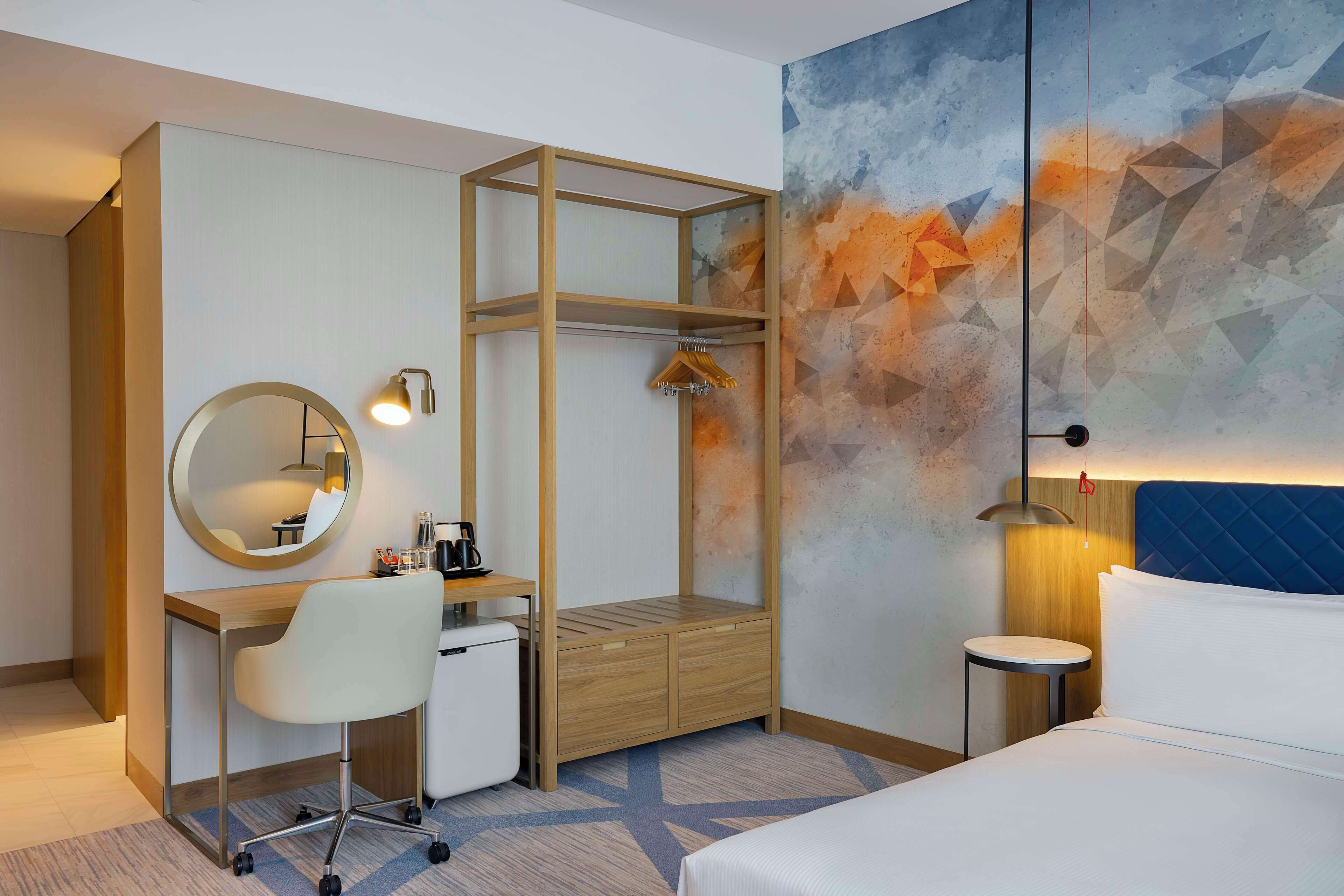 Habitación de hotel con escritorio, silla, cama y una obra de arte en la pared.