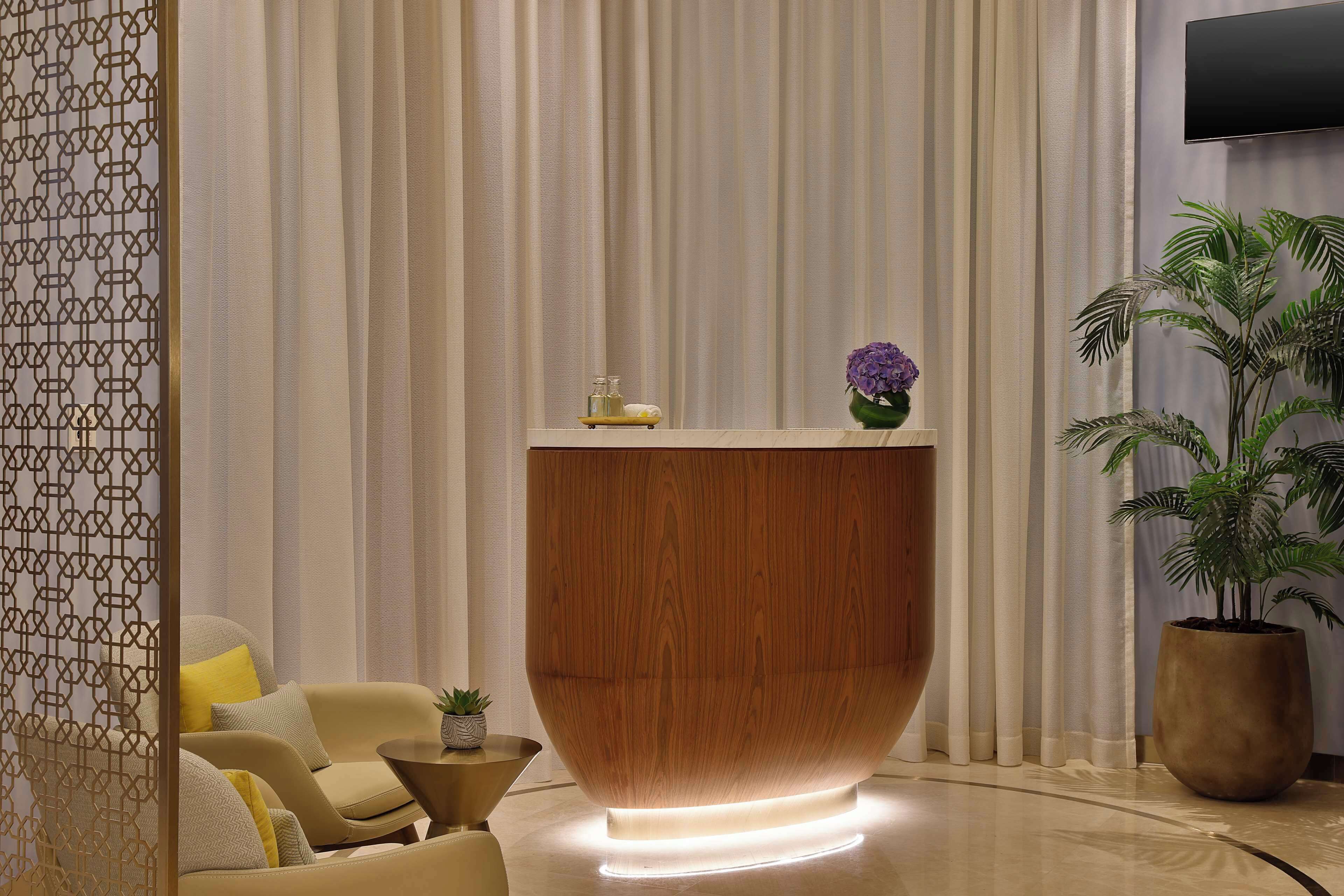 A modern reception desk with a wooden finish and a small vase of purple flowers on top.
