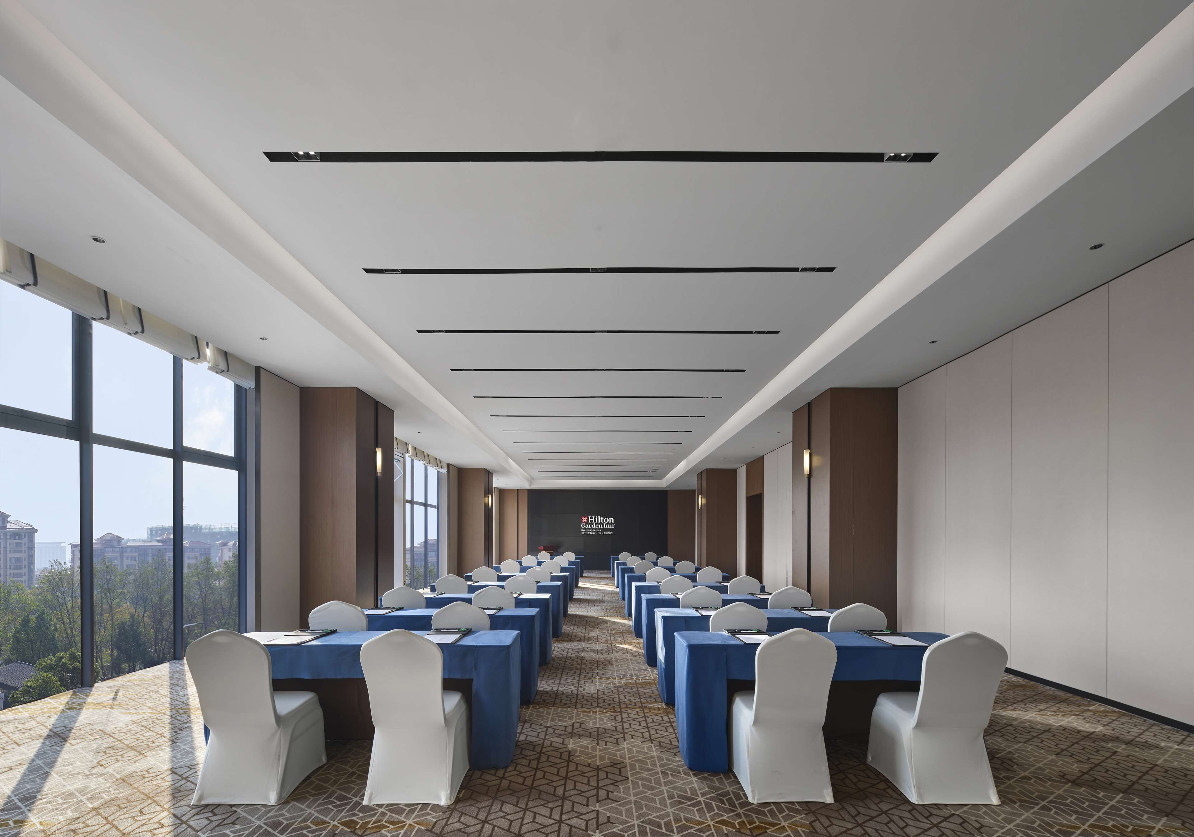 Une salle de conférence avec des rangées de tables et de chaises, de grandes fenêtres et une vue sur les bâtiments.