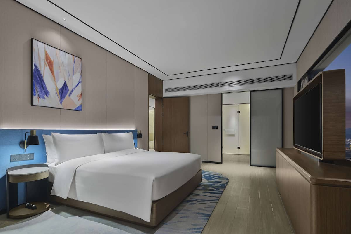 Een moderne hotelkamer met een groot bed, een flatscreen televisie, een nachtkastje en een schilderij aan de muur.