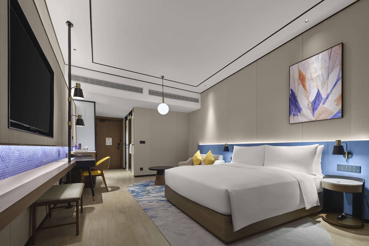 Een moderne hotelkamer met een groot bed, een bureau met stoel, een klein tafeltje en een televisie.