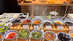 Un bufé con diversos alimentos en recipientes, un lavabo y utensilios de cocina al fondo.